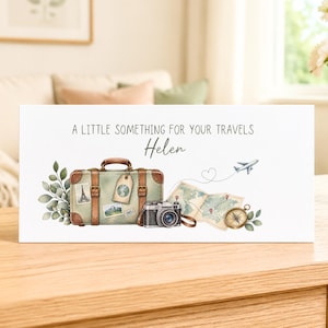 May include: A rectangular white sign featuring the text A LITTLE SOMETHING FOR YOUR TRAVELS and the name Helen. The illustration includes a vintage green suitcase with brown straps, a camera, a map, a compass, and a small aeroplane.