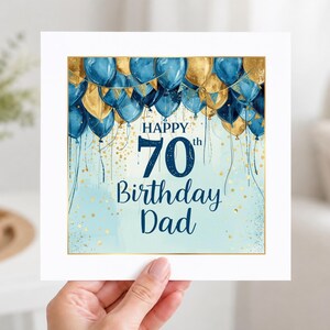 May include: A square greeting card featuring a festive design with blue and gold balloons at the top. The text reads Happy 70th Birthday Dad in dark blue lettering. The background is a light blue watercolor wash with gold confetti accents.