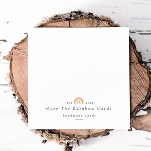 以下が含まれることがあります： 白地に「Over The Rainbow Cards」と「handmade cards」という黒い文字が書かれたカード。文字の上に小さな虹のグラフィックが描かれている。虹のグラフィックの上に「est 2022」という黒い文字が書かれている。