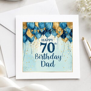 May include: A square greeting card featuring a watercolor illustration of blue and gold balloons at the top with gold confetti accents. The text reads Happy 70th Birthday Dad in dark blue script and block lettering against a light blue background.