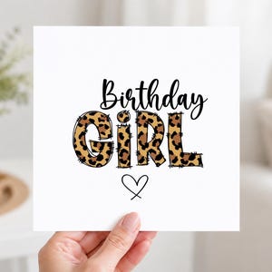 May include: A square white card featuring the black text Birthday above the word GIRL in a brown and black leopard print pattern with a stitched outline effect. Below the text is a simple black hand-drawn heart outline centred on the card.