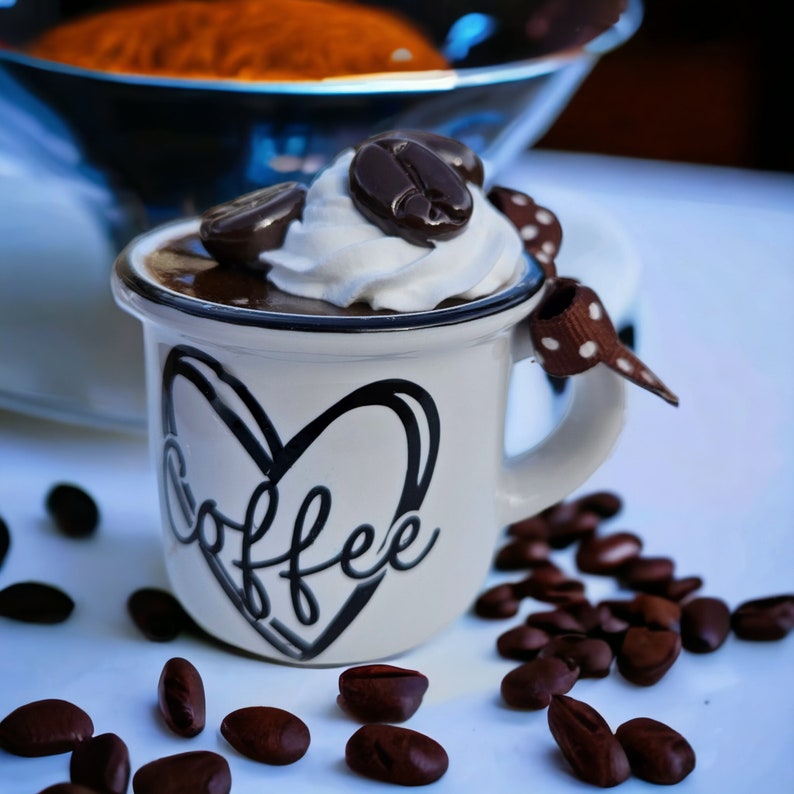 May include: A white ceramic mug with a black heart and the word "coffee" written inside. The mug is filled with chocolate mousse topped with whipped cream and a chocolate coffee bean.