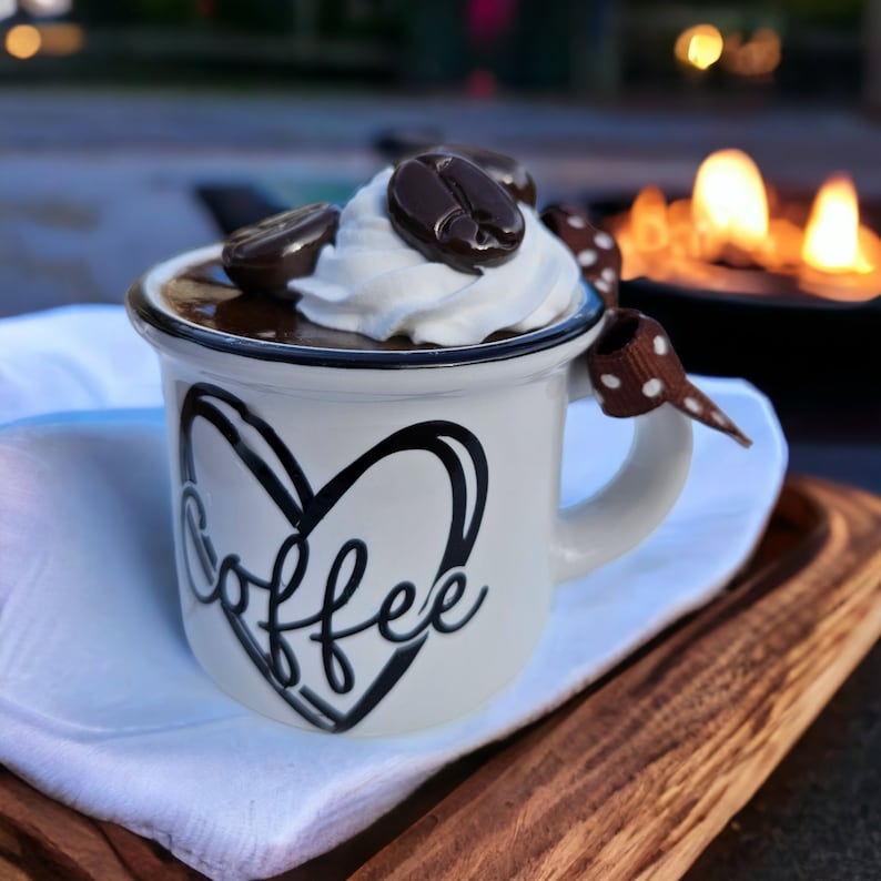 May include: A white ceramic mug with a black heart and the word "coffee" written inside. The mug is filled with chocolate mousse topped with whipped cream and chocolate coffee beans.