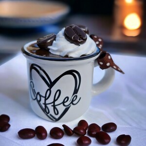 May include: A white ceramic mug with a black heart and the word "coffee" written inside. The mug is filled with chocolate mousse topped with whipped cream and chocolate coffee beans.