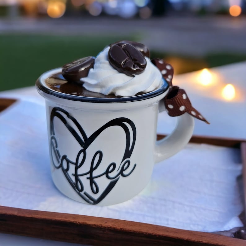 May include: White ceramic coffee mug with a black heart and the word "coffee" written inside. The mug is filled with chocolate mousse topped with whipped cream and chocolate coffee beans.