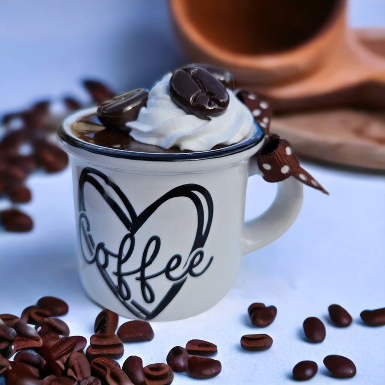 May include: A white ceramic coffee mug with a black heart and the word "coffee" written inside. The mug is filled with chocolate mousse topped with whipped cream and chocolate coffee beans.