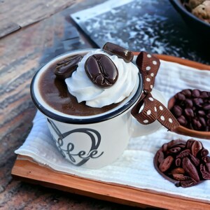 May include: A white ceramic mug with a black rim and the word "coffee" written on the side. The mug is filled with a brown liquid topped with whipped cream and chocolate coffee beans.