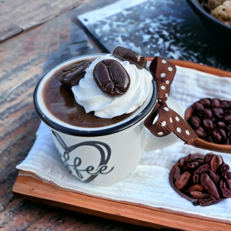 May include: A white ceramic mug with a black rim and the word "coffee" written on the side. The mug is filled with a brown liquid topped with whipped cream and chocolate coffee beans.