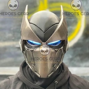 May include: A silver and black helmet with blue glowing eyes. The helmet has a sharp, angular design with a pointed top and a chin guard.