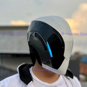 May include: A white and black helmet with a blue light strip. The helmet has a futuristic design and is being worn by a person wearing a white hoodie.