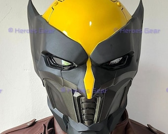 May include: A black and yellow plastic mask with a futuristic design. The mask has a yellow top and a black lower face with a detailed design. The mask has two green eyes.