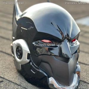 Könnte beinhalten: Schwarzer und silberner Batman-Helm mit roten Augen. Der Helm hat eine strukturierte Oberfläche und ein elegantes Design.