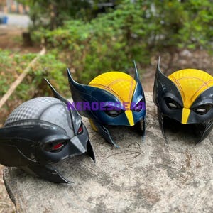 Puede incluir: Tres máscaras de Wolverine, una negra con ojos rojos, una amarilla y negra con ojos azules y una amarilla y negra con ojos morados.