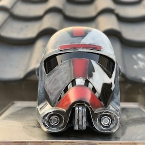 May include: A black and red helmet with a weathered, distressed look. The helmet has a visor and a red stripe down the center.
