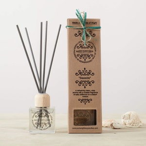 May include: A brown cardboard box with a clear window showing a glass bottle of reed diffuser with gray reeds. The box has a white label with the text "Reed Diffuser" and "Seaside".