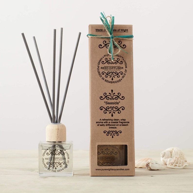 May include: A brown cardboard box with a clear window showing a glass bottle of reed diffuser with gray reeds. The box has a white label with the text "Reed Diffuser" and "Seaside".
