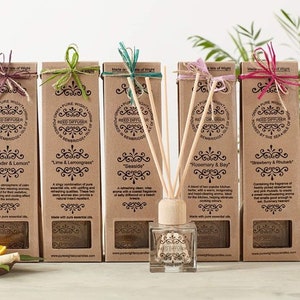 May include: A set of seven brown cardboard boxes containing reed diffusers. Each box features a different scent, including Lavender & Lemon, Lime & Lemongrass, Seaside, Rosemary & Bay, Strawberry & Rhubarb, Geranium & Orange. The boxes are displayed in a row on a wooden surface.