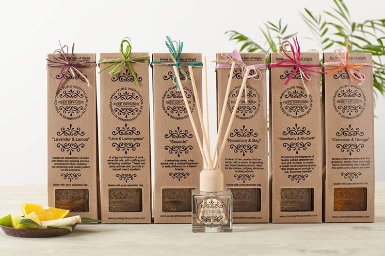 May include: A set of seven brown cardboard boxes with reed diffusers. Each box has a different scent, including Lavender & Lemon, Lime & Lemongrass, Seaside, Rosemary & Bay, Strawberry & Rhubarb, Geranium & Orange. The boxes are arranged in a row on a wooden surface.