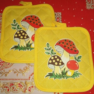 May include: Two yellow quilted pot holders with a mushroom design. The mushrooms are red, brown, and white with white spots. The pot holders have a quilted texture.