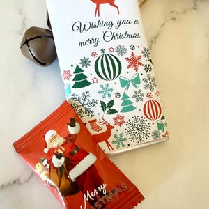 May include: A rectangular chocolate bar wrapper with a white background, a red reindeer silhouette, and the text Wishing you a merry Christmas, surrounded by green and red holiday icons. Below it, a red candy wrapper features Santa Claus.