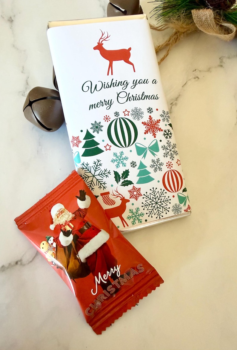 May include: A rectangular chocolate bar wrapper with a white background, a red reindeer silhouette, and the text Wishing you a merry Christmas, surrounded by green and red holiday icons. Below it, a red candy wrapper features Santa Claus.