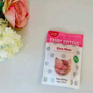 May include: A white and pink Candy Kittens Eton Mess gourmet sweets pouch featuring a cat-shaped clear window showing pink and white candies. The packaging includes text reading I'm carbon neutral, Candy Kittens, Eton Mess, Vegan Recipe, and 54g/1.9oz.