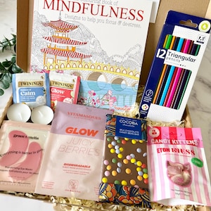 May include: A gift box containing The Colouring Book of Mindfulness, a pack of 12 triangular pencils, two Twinings tea bags, two tea light candles, pink Grace & Stella eye masks, a Vitamasques sheet mask, a Cocoba chocolate bar, and Candy Kittens.