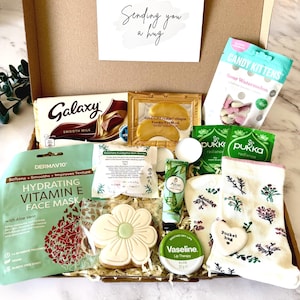 May include: A gift box containing a Galaxy chocolate bar, Candy Kittens sour watermelon sweets, a gold collagen eye mask, Pukka tea, a DermaV10 Vitamin E face mask, a flower-shaped biscuit, aloe hand cream, Vaseline lip therapy, and floral socks.