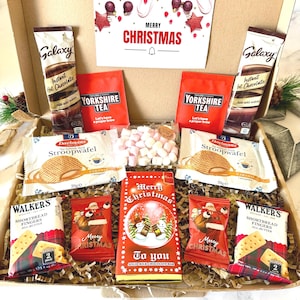 May include: A Christmas gift box containing two Galaxy instant hot chocolate packets, two Yorkshire Tea bags, two Daelmans stroopwafel packages, a bag of mini marshmallows, two Walker's shortbread finger packs, and a Merry Christmas chocolate bar.