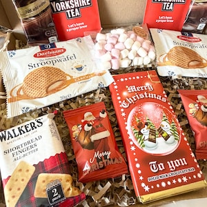 May include: A gift box containing two Taylors of Harrogate Yorkshire Tea bags, two Daelmans caramel stroopwafels, a Walker's shortbread fingers pack, a bag of mini marshmallows, a Merry Christmas chocolate bar, and hot chocolate mix.