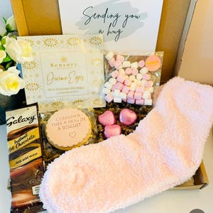 Letterbox Gift filled with pink fluffy socks, 3 mini heart chocolates, galaxy hot chocolate sachet, a self heating eye mask perfect for tired eyes and busy minds, a sending you a hug iced biscuit and a small bag of mini marshmallows. With the option to select from a gift card and add your own personalised message. Delivered straight to the recipient