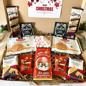 May include: A cardboard gift box containing two Galaxy instant hot chocolate packets, two Pukka English breakfast tea bags, two Daelmans stroopwafel packs, two Walkers shortbread finger packs, two small Santa-themed chocolate bags, and a Merry Christmas milk chocolate bar with a bag of mini marshmallows.