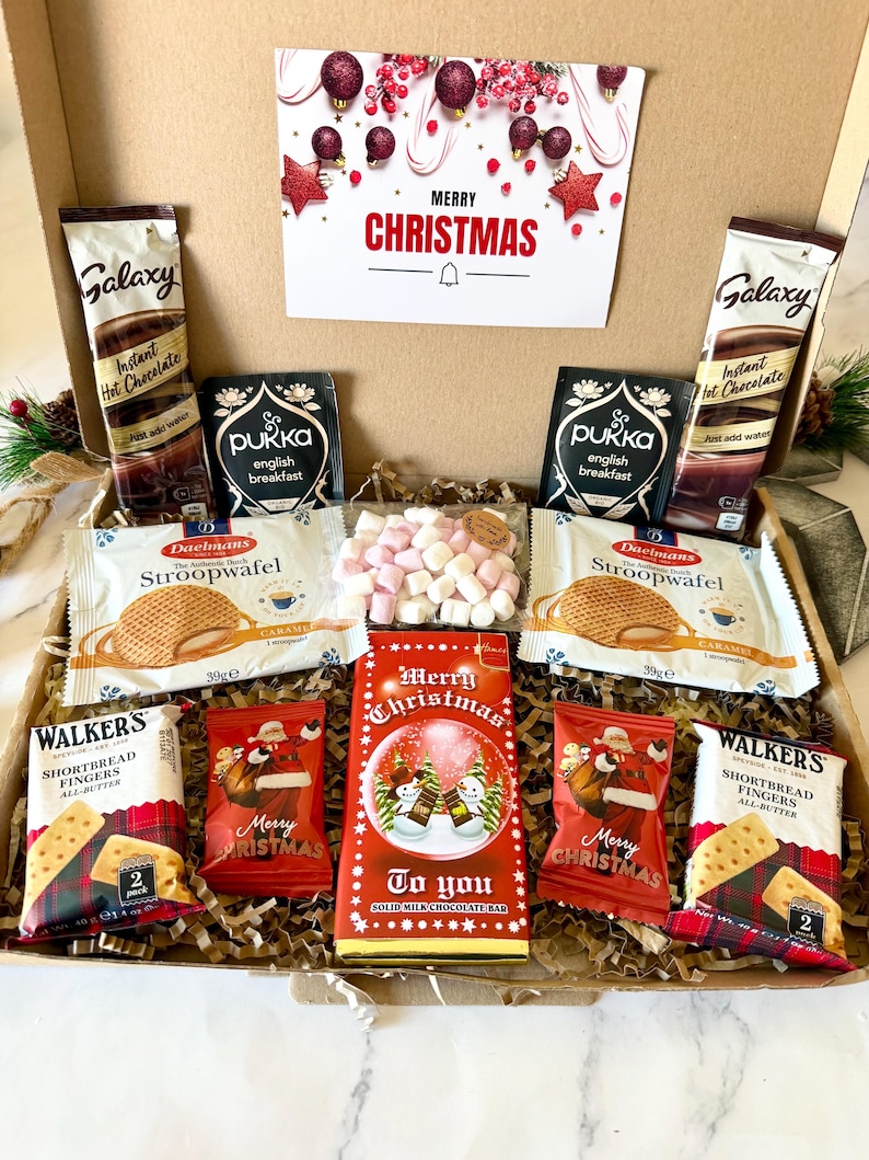 May include: A cardboard gift box containing two Galaxy instant hot chocolate packets, two Pukka English breakfast tea bags, two Daelmans stroopwafel packs, two Walkers shortbread finger packs, two small Santa-themed chocolate bags, and a Merry Christmas milk chocolate bar with a bag of mini marshmallows.