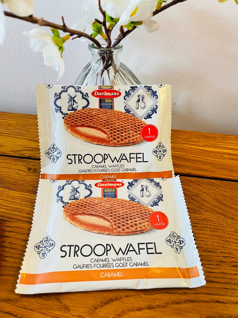 May include: Two individual Daelmans Stroopwafel packages featuring a graphic of a round, grid-patterned waffle with a caramel filling. The white packaging displays the text Stroopwafel, Caramel Waffles, and a red circle with 1 Waffle.