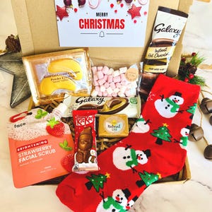 May include: A cardboard gift box containing a Merry Christmas card, a packet of Galaxy instant hot chocolate, a bag of mini marshmallows, a gold gel eye mask, a Galaxy chocolate bar, a KitKat Santa, a Natural Spa soap, and red socks with snowmen.
