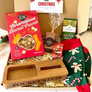 May include: A gift box containing a red box of Love Popcorn, a bag of double chocolate chip shortbread, a pack of Taylors Rich Italian coffee bags, a small Santa chocolate, green socks with gingerbread men, and a wooden tray labelled POCKET STUFF.