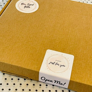 May include: A brown cardboard box with two stickers. One sticker says "Box Sized Gifts" in a circular design. The other sticker says "A Gift Just For You" and "Open Me!" in a rectangular design.