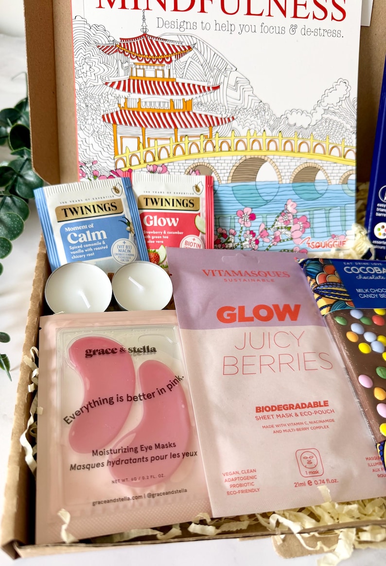 May include: A gift box containing a Mindfulness coloring book, Twinings Moment of Calm and Glow tea bags, two white tea light candles, Grace & Stella pink eye masks, a Vitamasques Juicy Berries sheet mask, and a Cocoba milk chocolate bar.