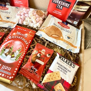 May include: A gift box filled with assorted treats including two red Taylors of Harrogate Yorkshire Tea packets, a Daelmans caramel stroopwafel, a Walkers shortbread fingers pack, a Merry Christmas chocolate bar, a Santa snack bag, and marshmallows.