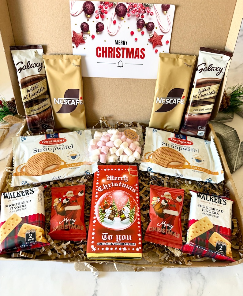 May include: A cardboard gift box containing two Galaxy instant hot chocolate packets, two Nescafe coffee sachets, two Daelmans stroopwafel packages, two Walker's shortbread finger packs, two Santa-themed chocolate bags, and a Merry Christmas chocolate bar.
