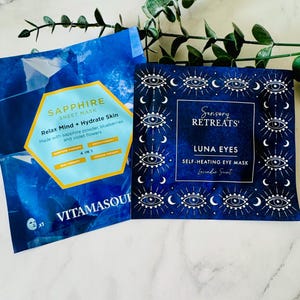 May include: Two blue face mask packets. One reads "SAPPHIRE SHEET MASK" with text about relaxing and hydrating skin. The other reads "Sensory RETREATS LUNA EYES SELF-HEATING EYE MASK Lavender Scent" with eye and crescent moon designs.