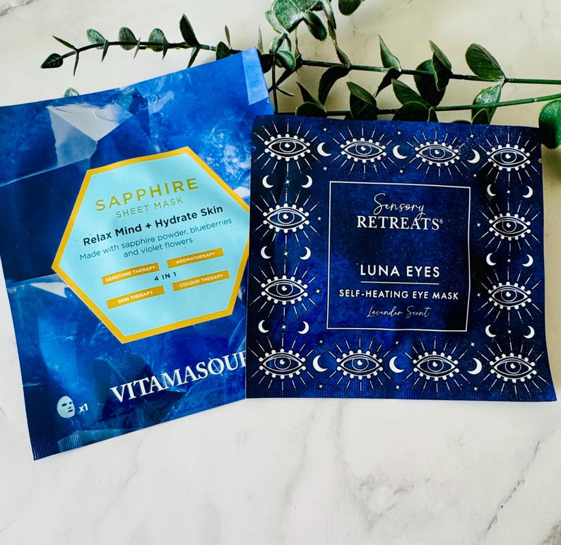 May include: Two blue face mask packets. One reads "SAPPHIRE SHEET MASK" with text about relaxing and hydrating skin. The other reads "Sensory RETREATS LUNA EYES SELF-HEATING EYE MASK Lavender Scent" with eye and crescent moon designs.