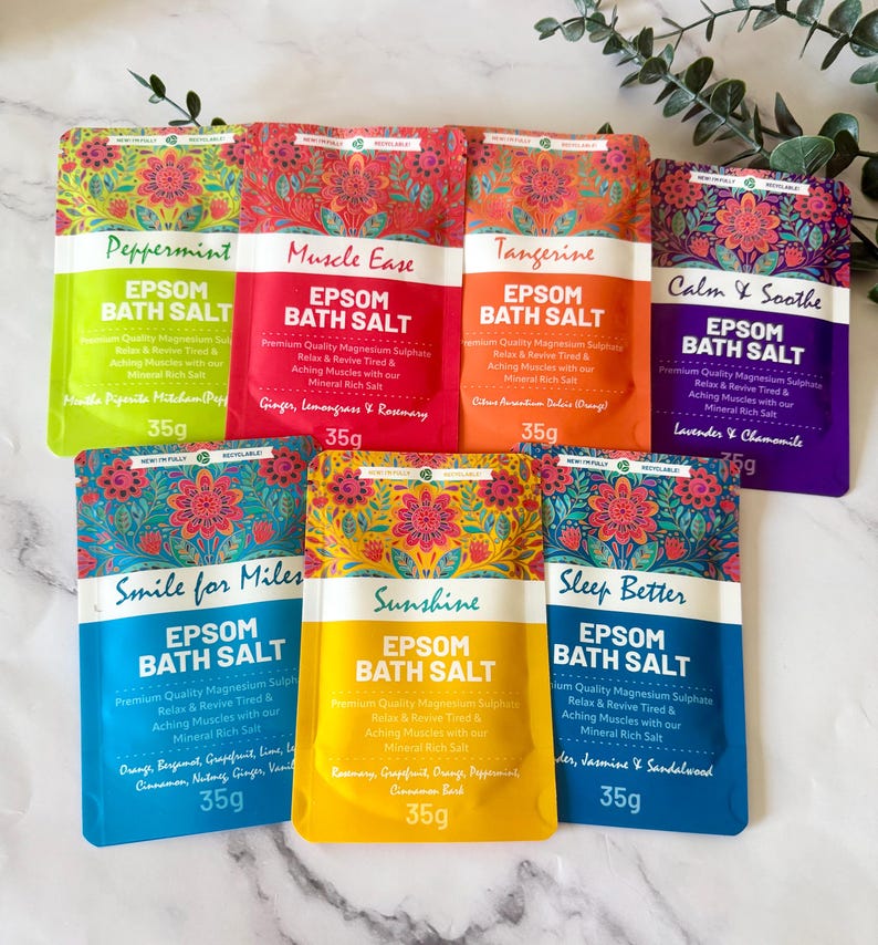 May include: Seven colourful 35g pouches of Epsom bath salt arranged in a group. Each pouch features a floral pattern at the top and text including Peppermint, Muscle Ease, Tangerine, Calm & Soothe, Smile for Miles, Sunshine, and Sleep Better.