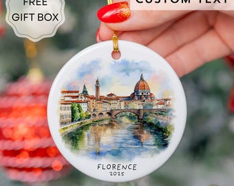 May include: A circular white ceramic Christmas ornament with a watercolour painting of Florence, Italy, and the text "FLORENCE 2025". It has a gold hanging string and the words "CUSTOM TEXT" are at the top.