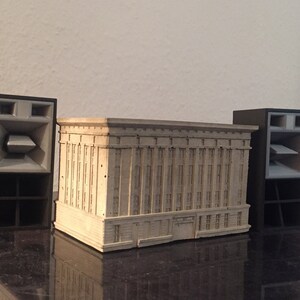 Peut inclure: Trois enceintes noires avec des cônes de haut-parleur gris. Les enceintes sont disposées en rangée sur une surface noire. Un petit modèle de bâtiment rectangulaire beige se trouve au centre des enceintes.