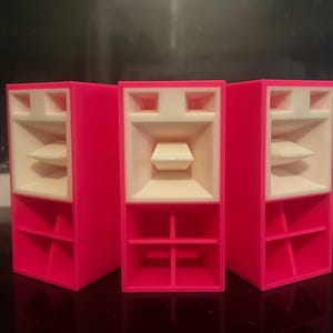 Peut inclure: Trois enceintes acoustiques roses avec des cônes de haut-parleur blancs. Chaque enceinte a une forme rectangulaire avec plusieurs compartiments.