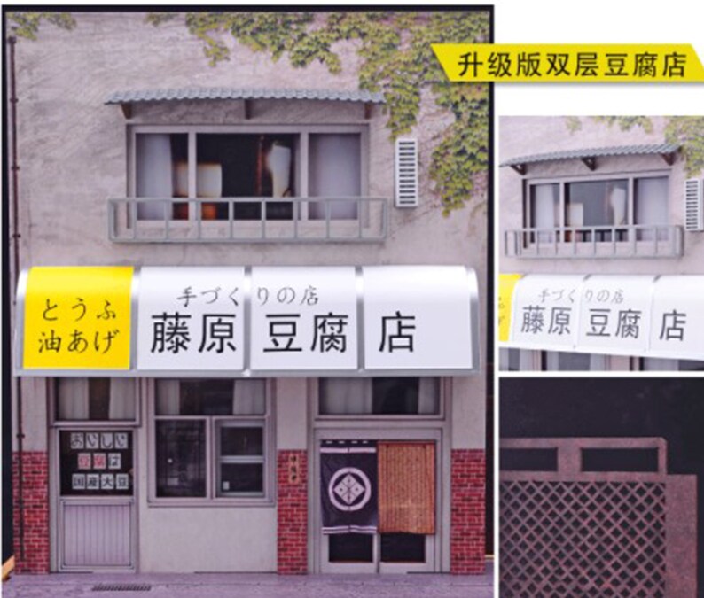 May include: A model of a Japanese tofu shop with a yellow awning that reads "とうふ 油あげ 藤原豆腐店" (tofu, oil-fried tofu, Fujiwara Tofu Shop). The shop has a red brick facade and a traditional Japanese door with a black and white design.