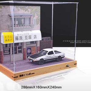 May include: A white diecast car model with black accents and the text "藤原豆腐店" on the side, displayed in a clear acrylic case with a wooden base. The case also includes a miniature building with a sign that reads "とうふ 油あげ 藤原豆腐店". The case measures 286mm x 160mm x 240mm.