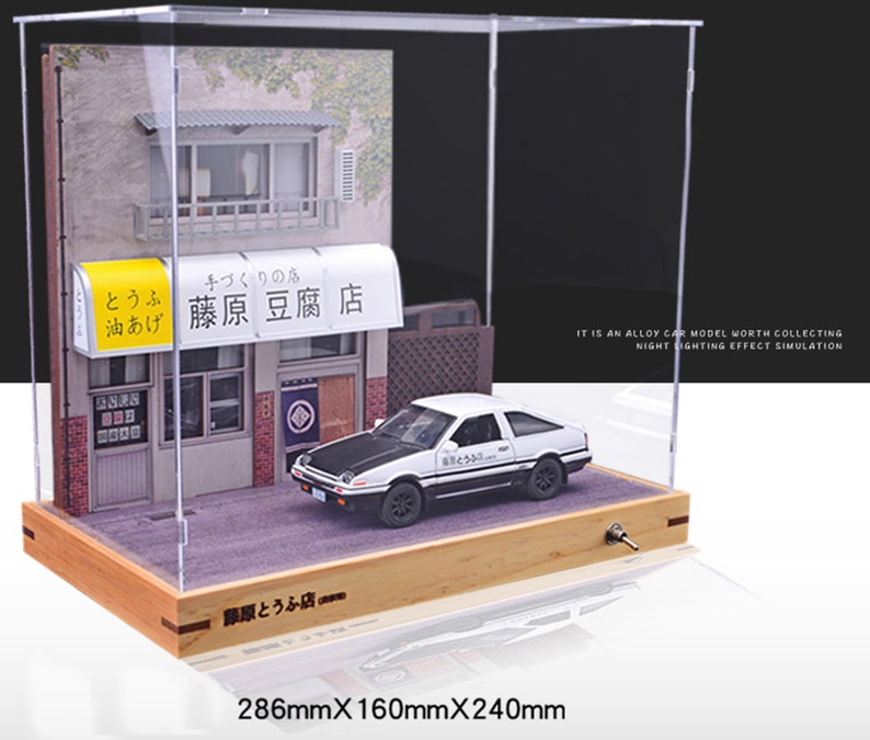 May include: A white diecast car model with black accents and the text "藤原豆腐店" on the side, displayed in a clear acrylic case with a wooden base. The case also includes a miniature building with a sign that reads "とうふ 油あげ 藤原豆腐店". The case measures 286mm x 160mm x 240mm.
