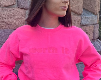 May include: A bright pink sweatshirt with the text "worth it" in a raised, pink font.